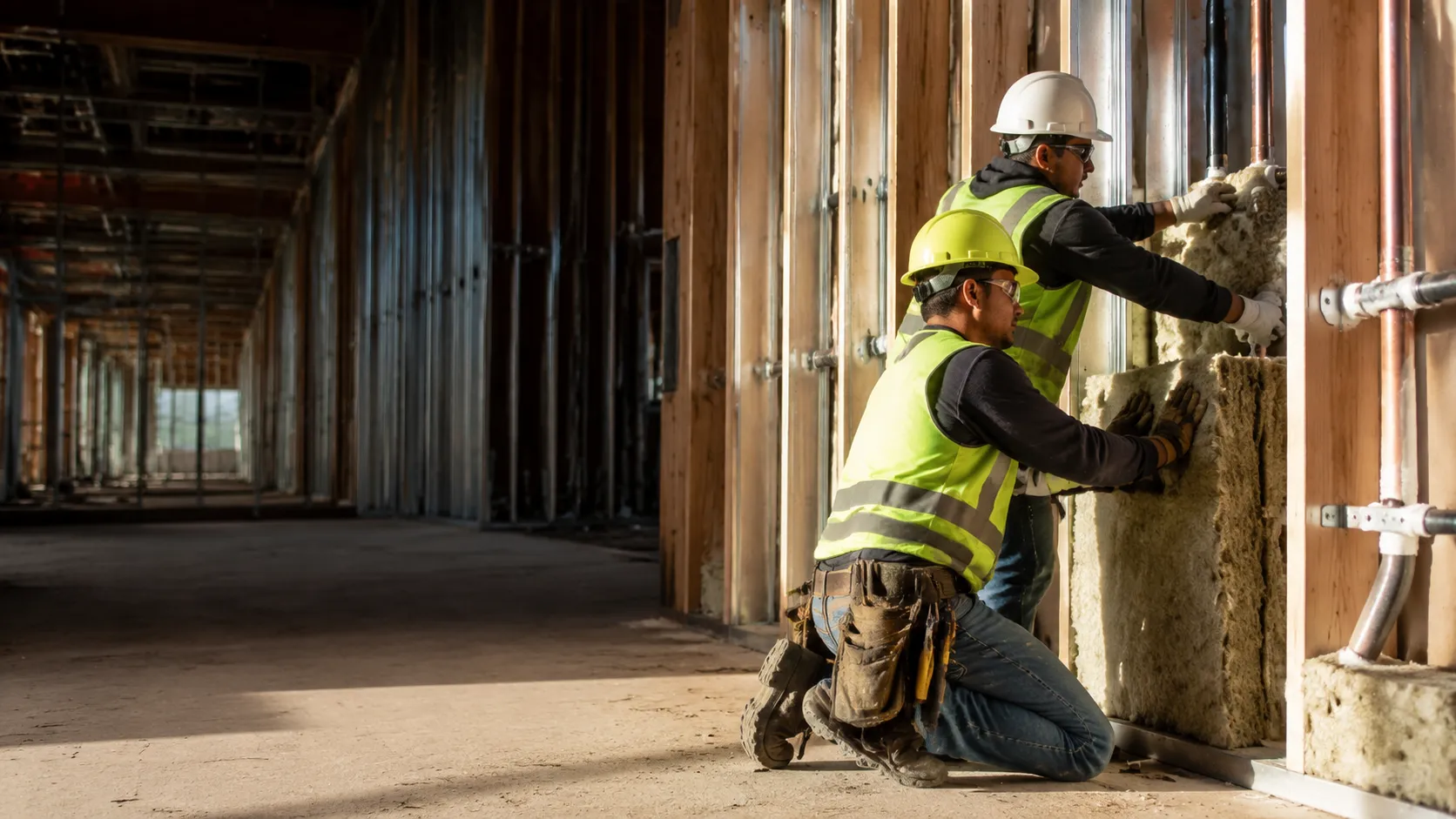 Insulation crew packing fire-rated mineral wool batt into a framed fire-rated wall around pipe penetrations on a commercial multi-unit site in Abbotsford — commercial fire stop insulation Abbotsford